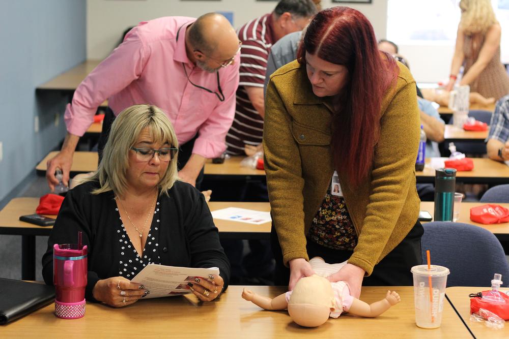 two employees consult manual to learn how to properly perform chest compressions on an infant