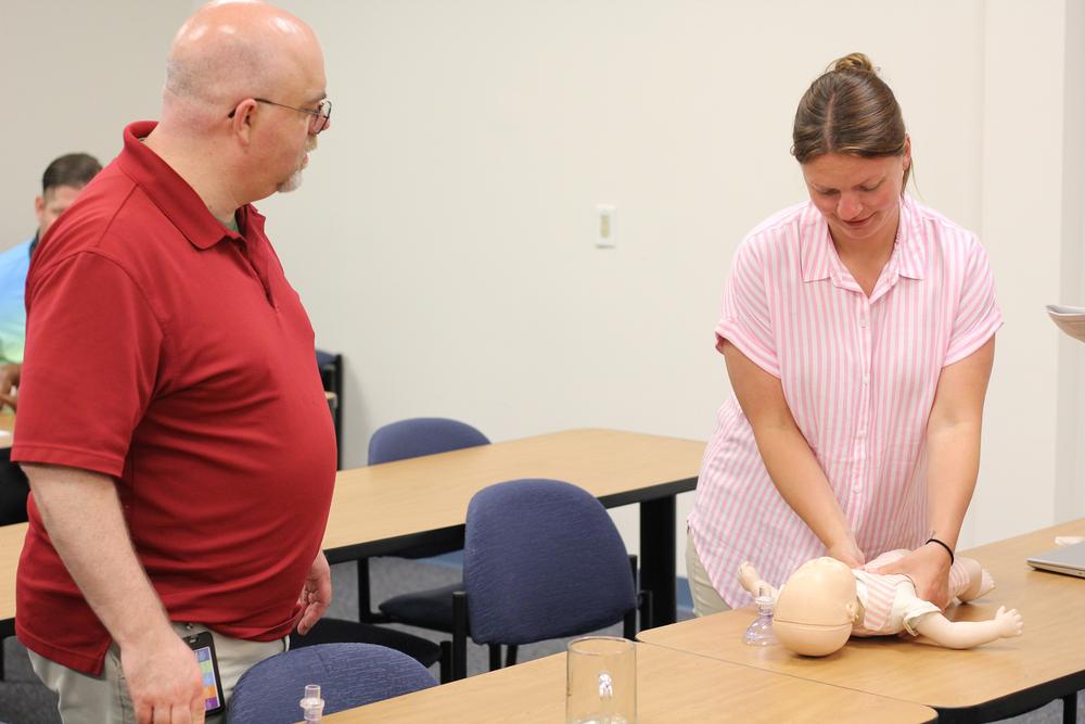 two different cnyic employees converse about how to best perform chest compressions on an infant
